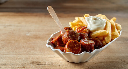 Delicious curried sausage chunks with fries and sauces in bowl - 441362701