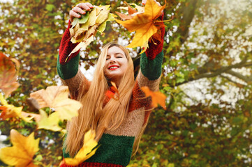 Joyful girl throws leaves in autumn park. Woman feel good outdoors in fall. Happy smiling person in nature background