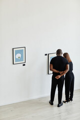 Minimal wide angle view at elegant couple looking at paintings in modern art gallery, copy space