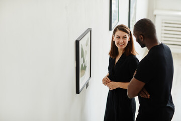 Fototapeta premium Side view portrait of elegant couple looking at abstract paintings in modern art gallery, copy space