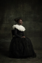 Medieval African young woman in black vintage dress with big white collar posing isolated on dark...