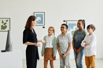 Diverse group of children listening to female expert while visiting modern art gallery, copy space