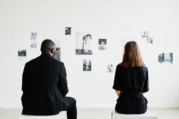 Minimal back view at elegant couple looking at black and white photographs in modern art gallery, copy space