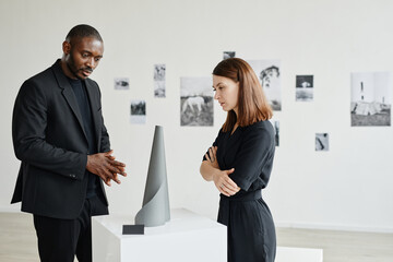 Side view portrait of elegant mixed-race couple wearing black in modern art gallery, copy space