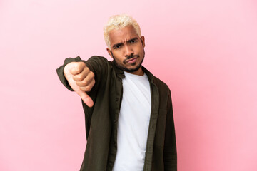 Young Colombian handsome man isolated on pink background showing thumb down with negative expression