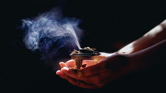 incense in a woman hand, incense smoke on a black background.