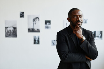Minimal waist up portrait of elegant African-American man wearing black while looking at photographs in modern art gallery, copy space