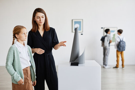 Portrait of mother and daughter looking at sculptures in modern art gallery, copy space