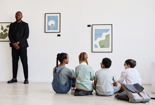 Diverse group of children sitting on floor in modern art gallery and discussing paintings, copy space