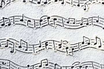 Musical notes pattern printed on white flour sand, powder on dark table. Natural, organic...