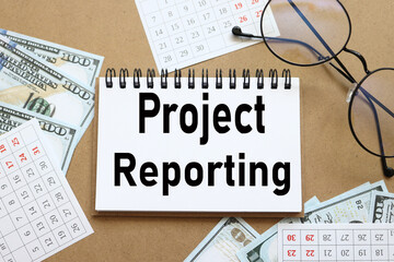 Project Reporting . text on white notepad paper near calendar on wood craft background