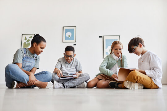 Diverse group of children sitting on floor in art gallery and discussing paintings