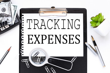 Tracking Expenses. text on a white sheet of paper near a magnifying glass m flowerpot in a pot