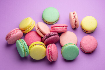 Colorful sweet macarons or macaroons, flavored cookies on purple background.