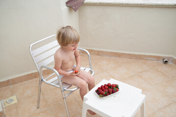 White child eats strawberries in summer sitting outdoors