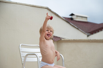 Funny child eats strawberries in summer sitting on the terrace on the background of the roofs