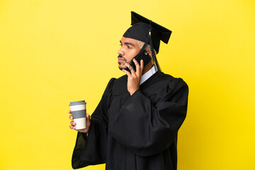 Young university graduate Colombian man isolated on yellow background holding coffee to take away and a mobile