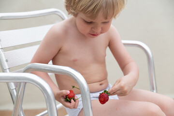 White child eats strawberries in summer sitting on the chair