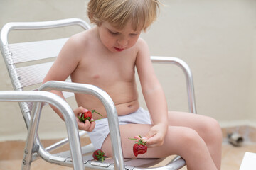 Caicasian child eats strawberries in summer sitting on the chair