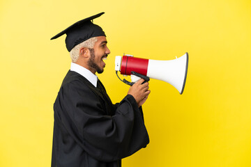 Young university graduate Colombian man isolated on yellow background shouting through a megaphone