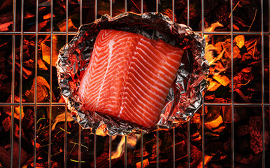 Salmon in aluminum foil on bbq grate over hot pieces of coals. Top view.