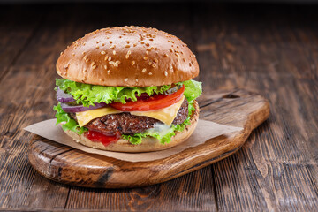 Delicious hamburger on a wooden table with a dark brown background behind. Fast food concept.