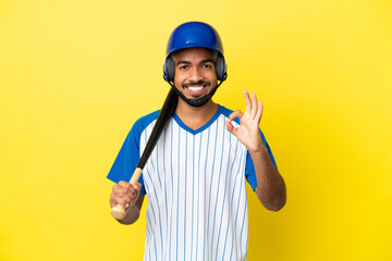 Young Colombian latin man playing baseball isolated on yellow background showing ok sign with fingers