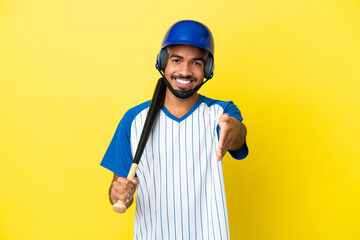 Young Colombian latin man playing baseball isolated on yellow background shaking hands for closing a good deal