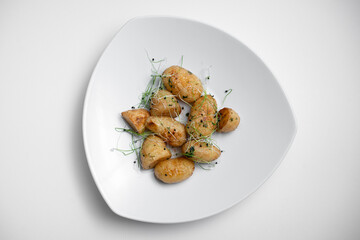 top view of tasty roasted potatoes with microgreen on plate on white background