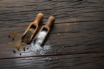 Sea salt and ground pepper in the wooden spoons on old wooden background. Two most popular...