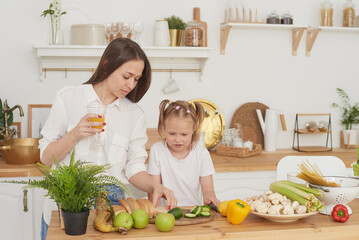 Mom and daughter prepare a salad in the kitchen. Happy loving family are preparing together. The...