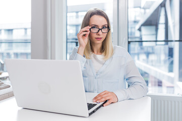 Caucasian happy young freelancer woman sitting at table and talking online on webcam remotely. Female student tells and communicates video call with friends or family indoors. Home or modern office