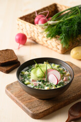 Homemade summer Okroshka soup with kefir served with rye bread and fresh vegetables on wooden table. Close up. Vertical format. Traditional Okroshka soup is Russian and Ukrainian cuisine for summer