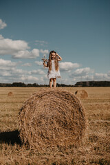 Naklejka na ściany i meble Adorable little girl in a field with haystacks.
