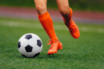 Soccer player hits the ball on the artificial turf. Footballer in sports cleats kicking ball. Legs...