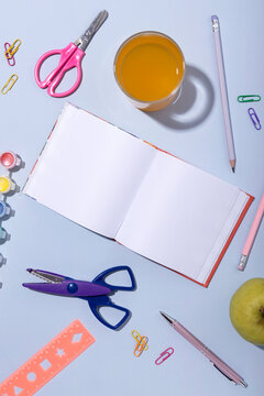 Vertical image of blank notebook,scissors,orange juice,apple,pens,pencils,ruler on the blue surface.Empty space.Back to school