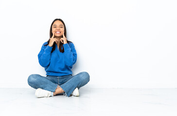 Young mixed race woman sitting on the floor isolated on white background smiling with a happy and pleasant expression