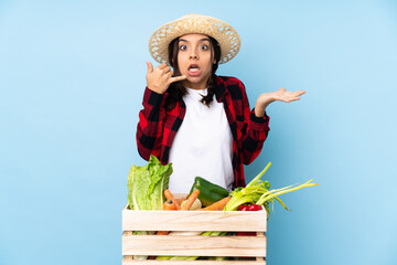 Young farmer Woman holding fresh vegetables in a wooden basket making phone gesture and doubting