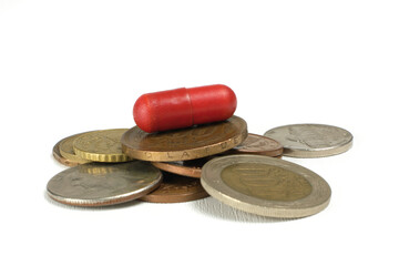 Pile of coins and red pill on them on a white background, close up.