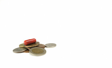 Pile of coins and red pill on them on a white background.