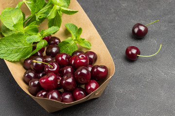 Sweet cherries and mint leaves in cardboard plate.
