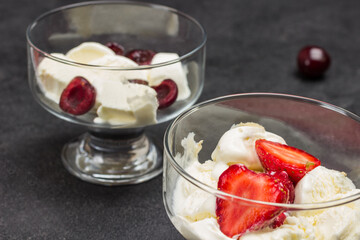 Two Ice-cream bowls with ice cream and berries. Cherry on table