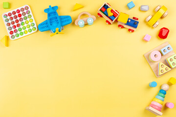 Baby kids toys background with wooden blocks, train, car, plane, pop it fidget toys on yellow background. Top view, copy space