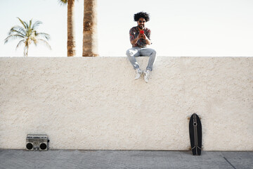 African man listening music with vintage boombox stereo outdoor while using mobile phone - Focus on...