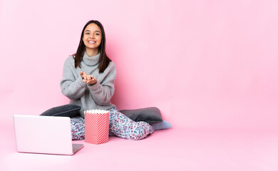 Young mixed race woman eating popcorn while watching a movie on the laptop holding copyspace imaginary on the palm to insert an ad