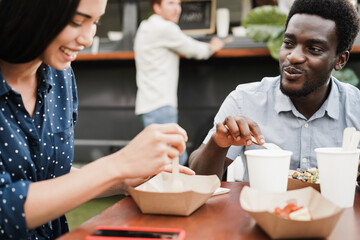 Fototapeta na wymiar Multiracial couple having fun eating at food truck restaurant outdoor - Focus on african american man face