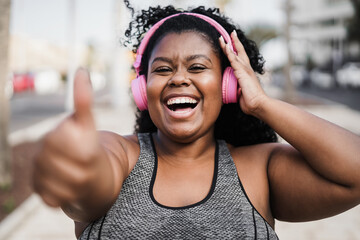 Happy sport curvy black girl listening music with headphones while doing jogging outdoor - Focus on...