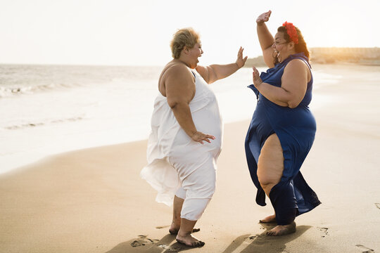 Curvy women friends dancing on the beach having fun during summer travel vacation - Focus on faces