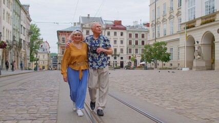 Senior stylish tourists man woman walking along street, looking for way using paper map in old town Lviv, Ukraine. Elderly travelers grandmother, grandfather getting lost in big city. Summer vacation