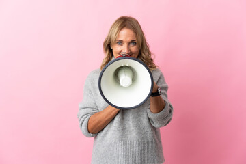 Middle aged blonde woman over isolated pink background shouting through a megaphone to announce something